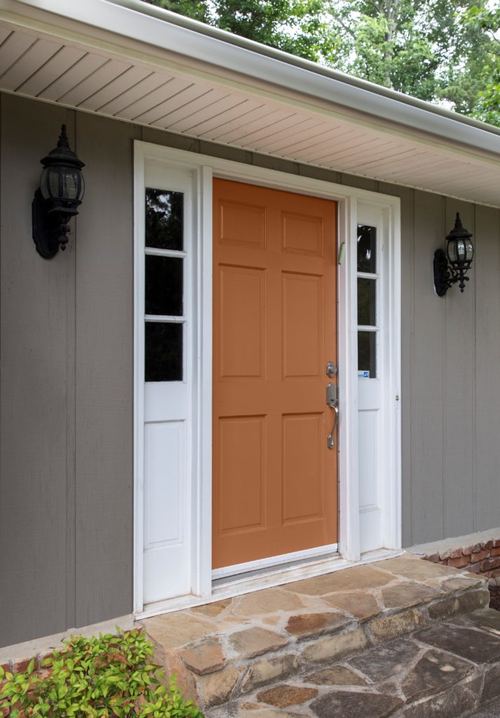 A mid range image of the front of a single family home.  The body of the house is painted in a mid-to-dark green with a green undertone called, Barnwood Gray.  The trim is featuring a super white color called ULTRA PURE WHITE.  The front main door features an inviting orange tone called Maple Glaze. 