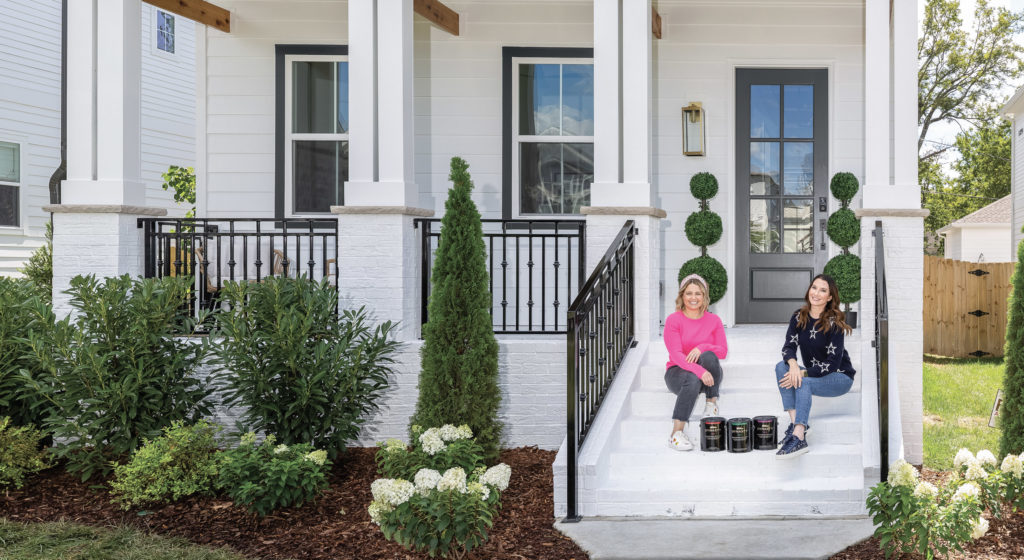 A picture of a home exterior and,  Clea Shearer and Joanna Teplin from the hit Netflix show sitting on the door steps of their new headquarters.  Three cans of BEHR Dynasty paint also on the door steps. 