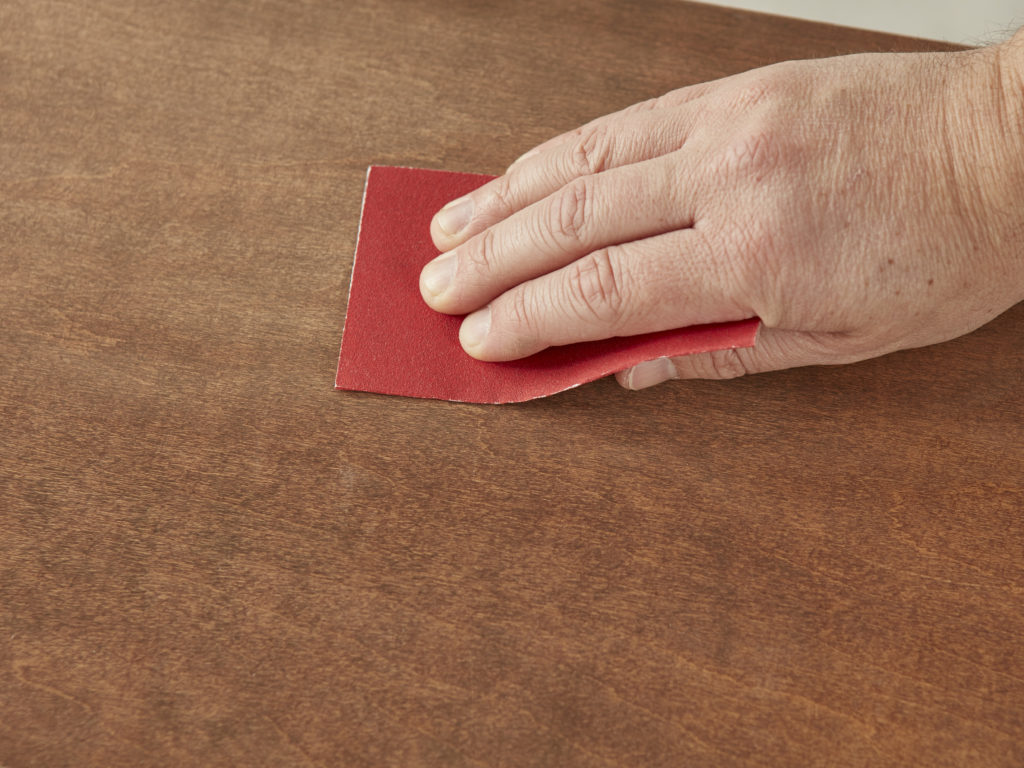 A person using sandpaper to smooth the top of a surface.