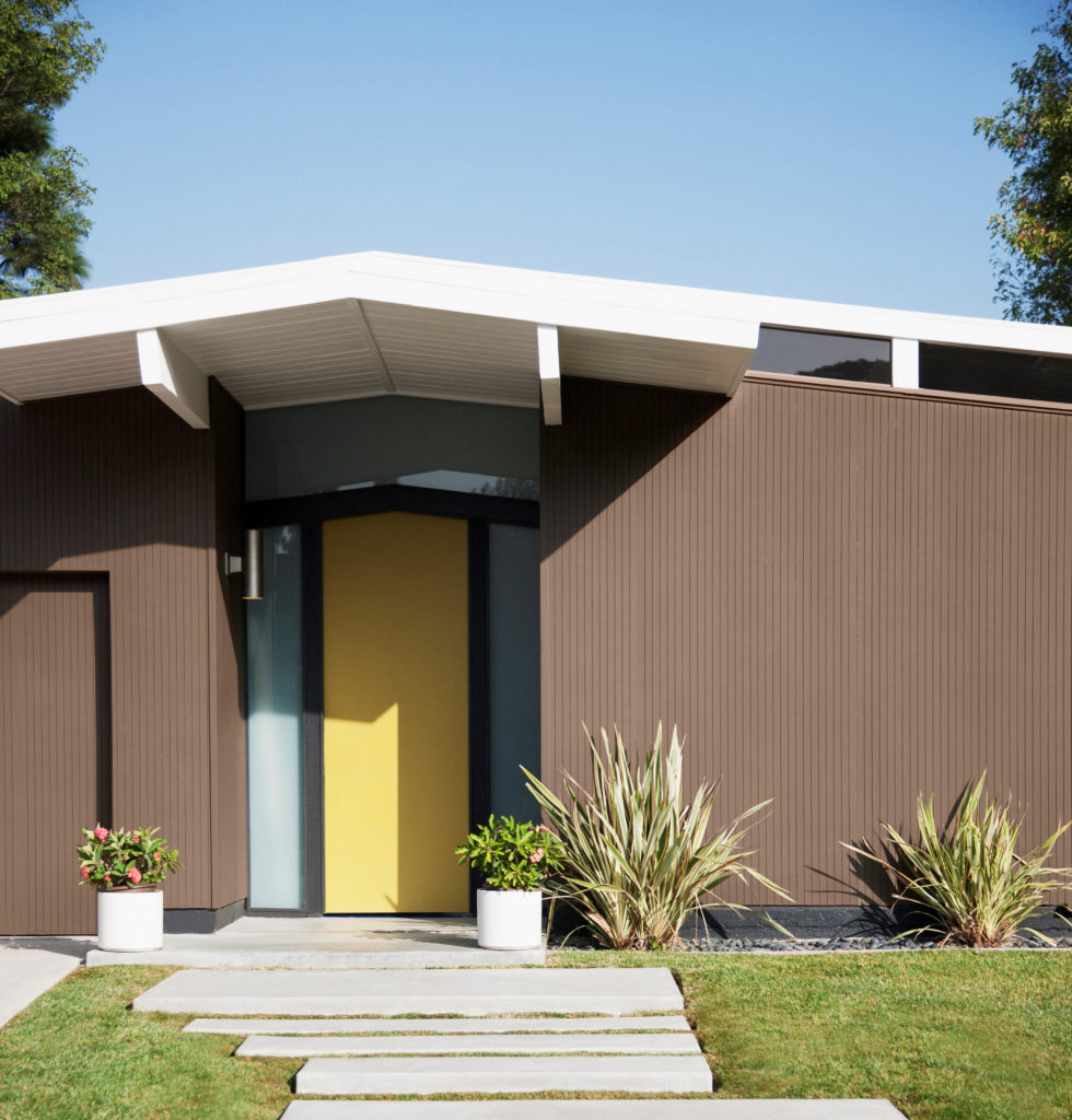 A Mid Century house, the house body is painted in a grounding brown color called Wild Mustang.  The front door is painted in a cheery bright yellow color.  Nice, manicured landscape. 
