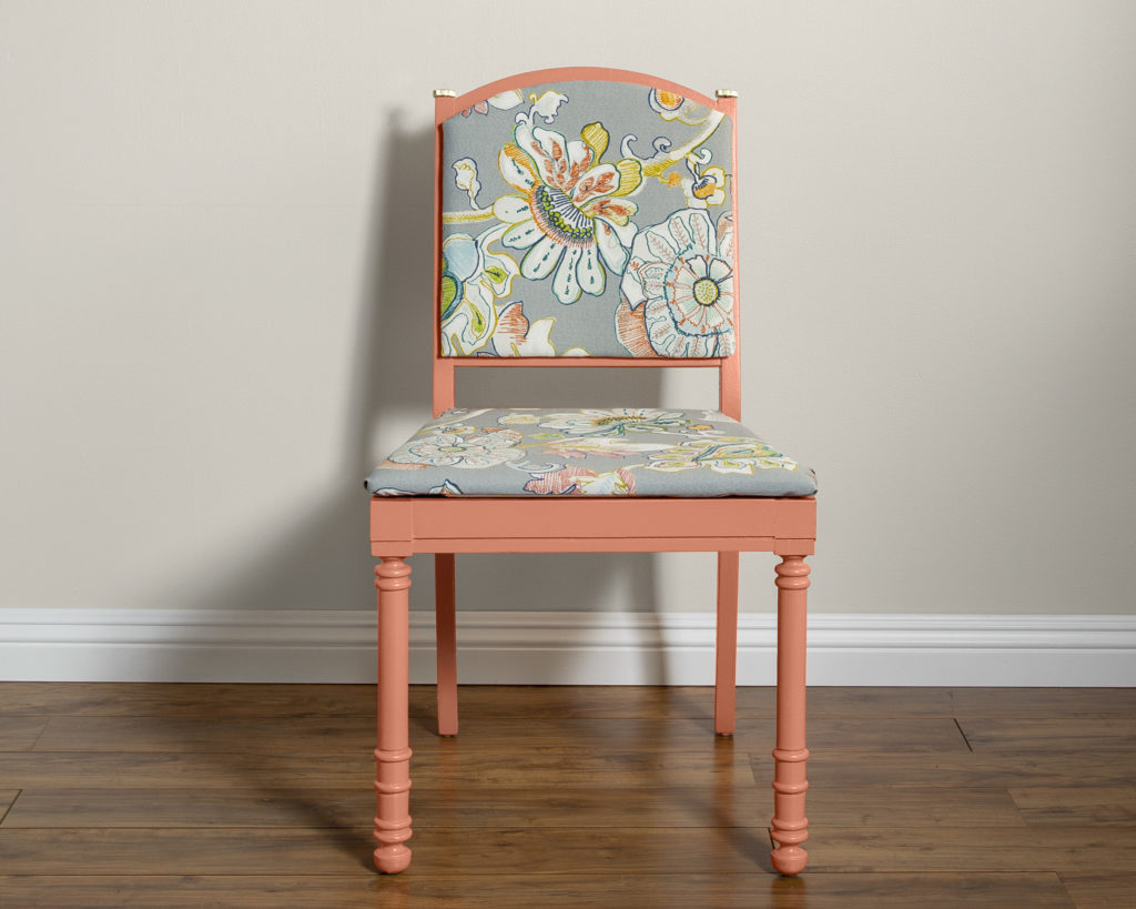 A chair painted in a muted coral and upholstered in a lively floral pattern.