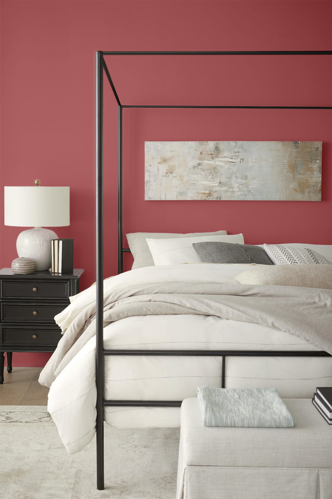 A contemporary bedroom with black furniture and the red walls.  The bedding is white and light beige and gray neutral tones. The walls are painted in a red color called Lingonberry Punch.