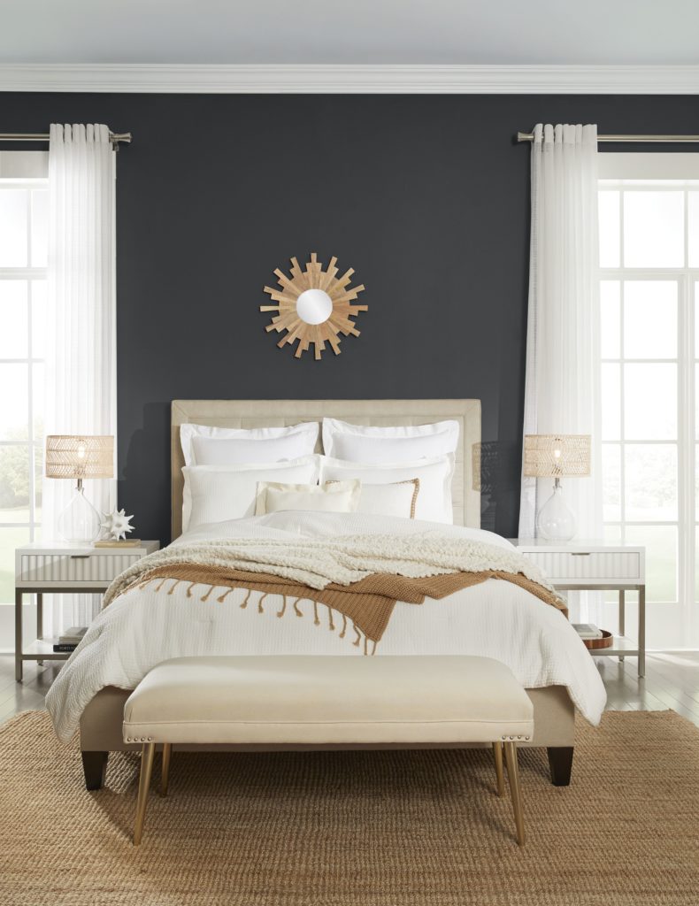 Bedroom image with accent wall in Cracked Pepper. Bed has white and brown furnishings, two side tables and lamps as well as a burlap rug below the bed. 