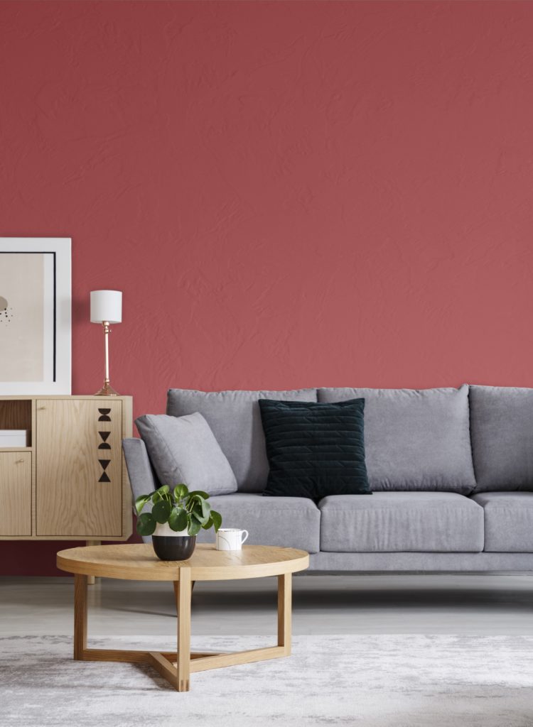 A red wall in an elegant living room interior with a sofa and round table, the color used on the wall is called Lingonberry Punch. 