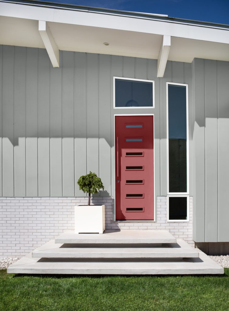 The exterior of a modern house, the house is painted in a light gray color.  The door is painted in a red color called Lingonberry Punch. 