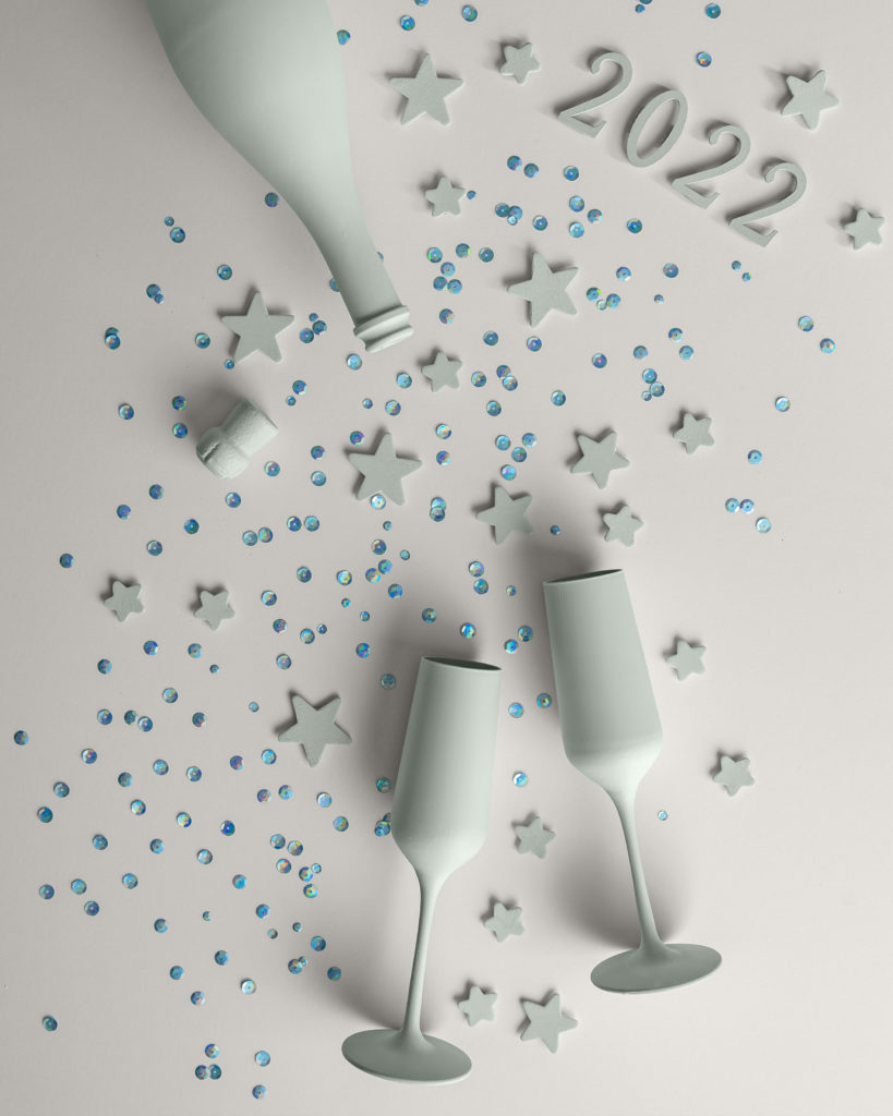 Table top image of painted champagne bottle and wine glasses in our Color of the Year Breezeway. Also painted are the number 2022 and stars. Blue confetti rhinestones also cover the table.