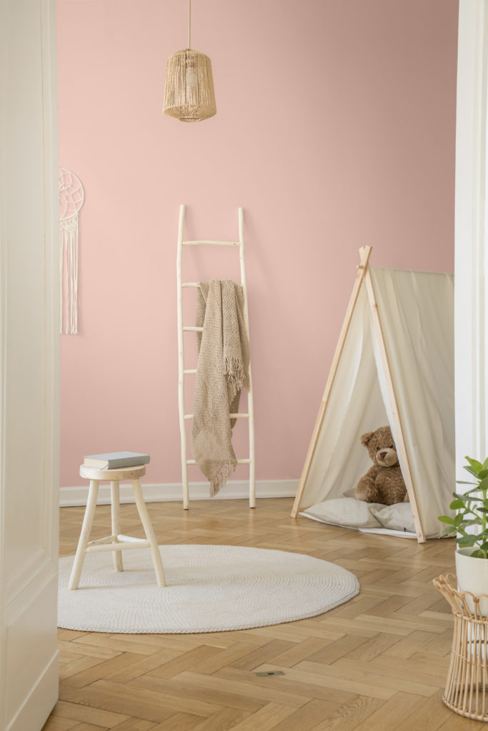 The vertical view of white Scandinavian nursery with tent, teddy bear and wooden ladder with beige blanket, real photo. The back wall is painted in a light pink paint color. 