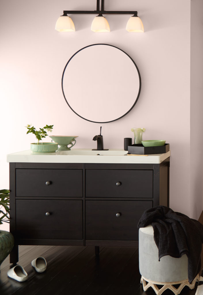Bathroom image that showcases sink vanity. Decor in sage green accents. 
Circular mirror and walls painted in Stolen Kiss a delicate light rose tone.