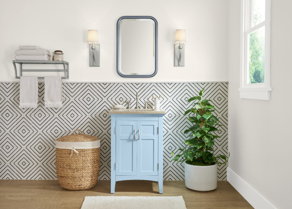 A bathroom with a small vanity painted in a light blue color. The lower accent wall is tiled with a geometric black and white design. 