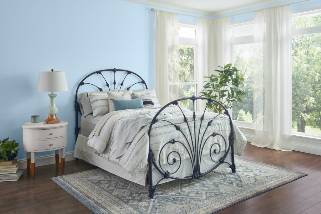 A vintage style bedroom, walls are painted in a pastel blue color called After Rain.  The bed frame is ornamental metal. 