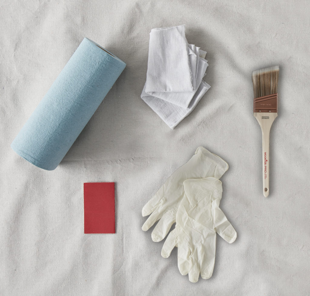 An image of tools used for a stain project; shop cloths, rags, brush, gloves, sandpaper.
