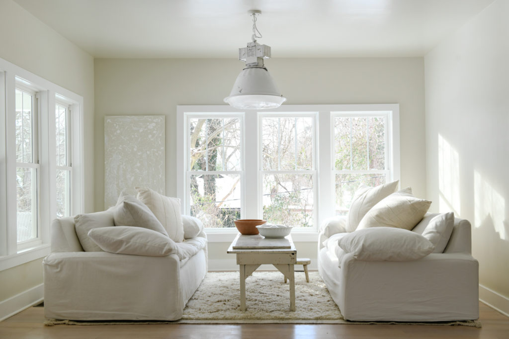 An all white living room with two couches facing each other and a long thin wood table between them.