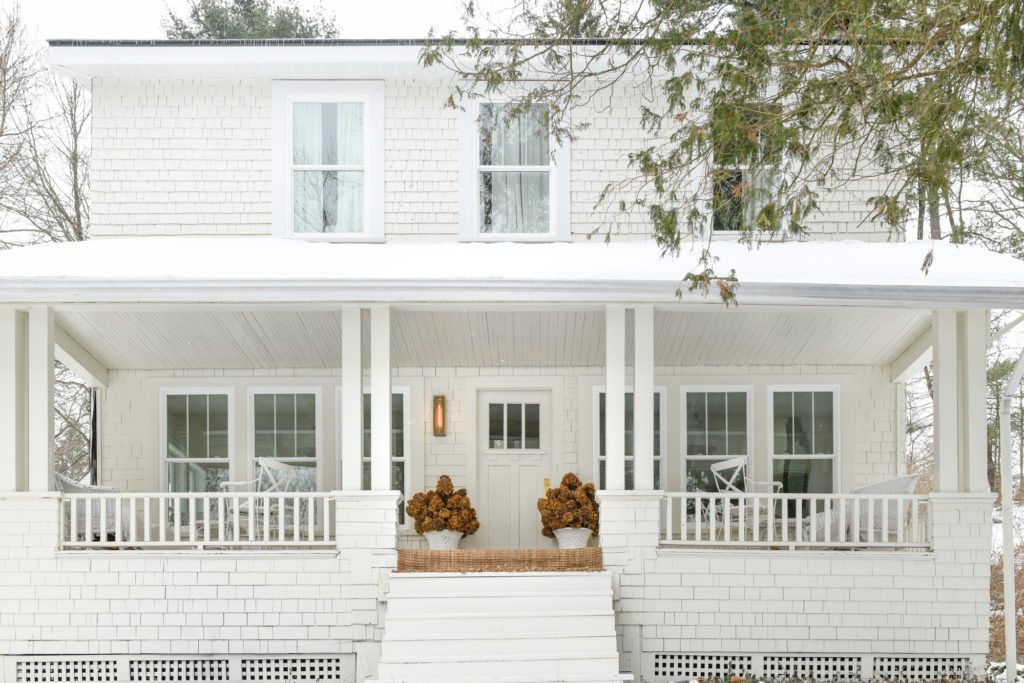 The front porch of an all white home with a touch of golden hues coming from flowers and an entry rug.