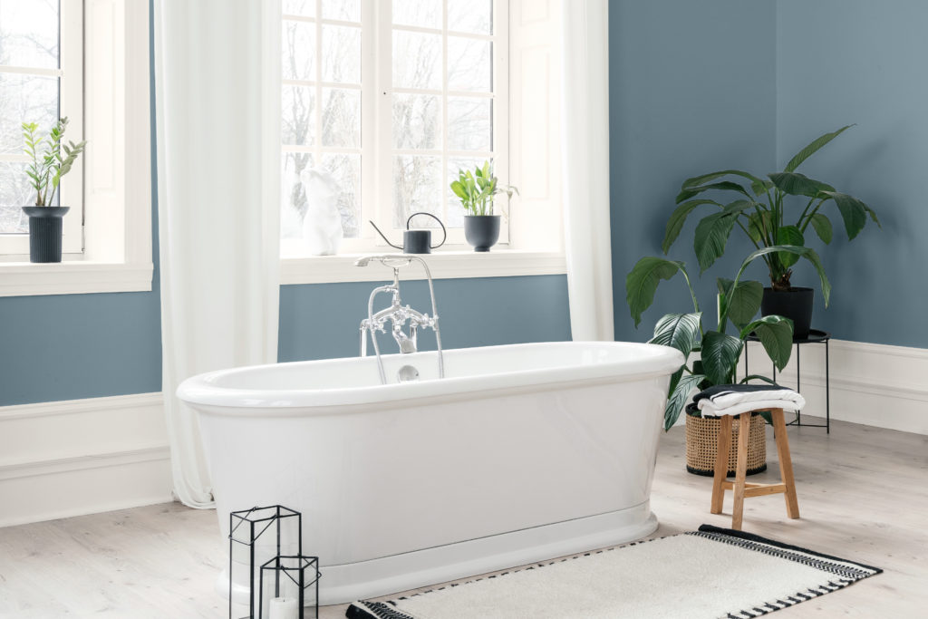 Bathroom image painted in Rainy Season a blue inspired by the spring rainstorms. Features plants, free standing tub and a calming atmosphere. 