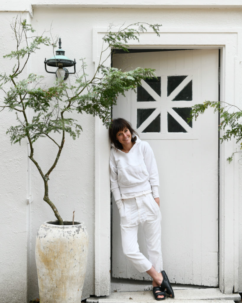A person leaning against an entryway. She is dressed in all white and the home is painted in all white.