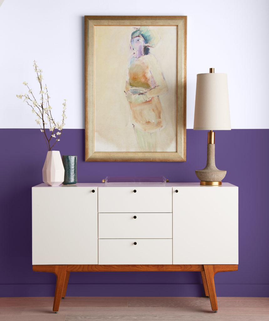 A console table sitting in front of a wall with the bottom half painted in a bold purple color and top painted in a soft white lavender.