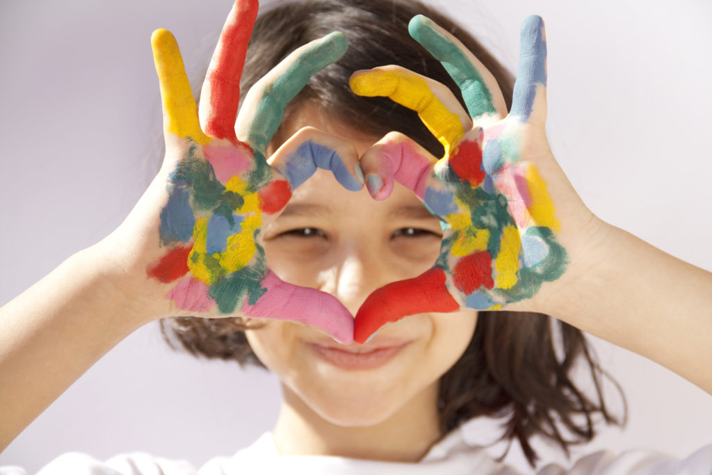 A girl holding her painted hands in a heart shape in front of her face.