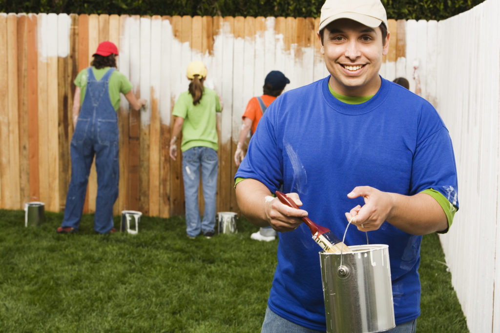 A group of people painting a wood fence.