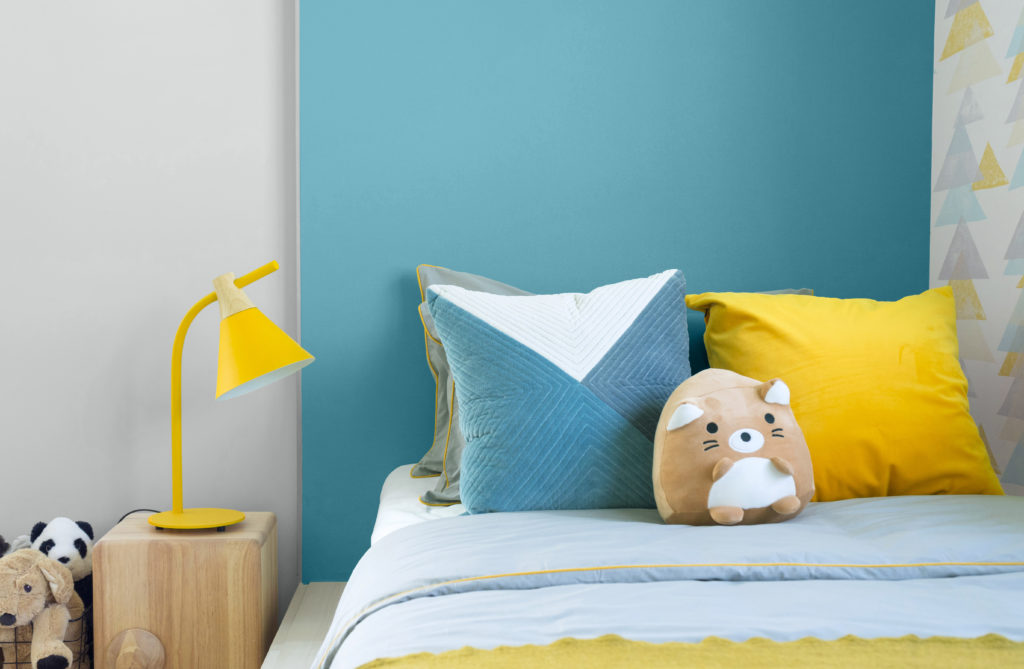 A modern blue kid's bedroom. Many dolls setting on bed with blue and yellow pillows in kid bedroom.