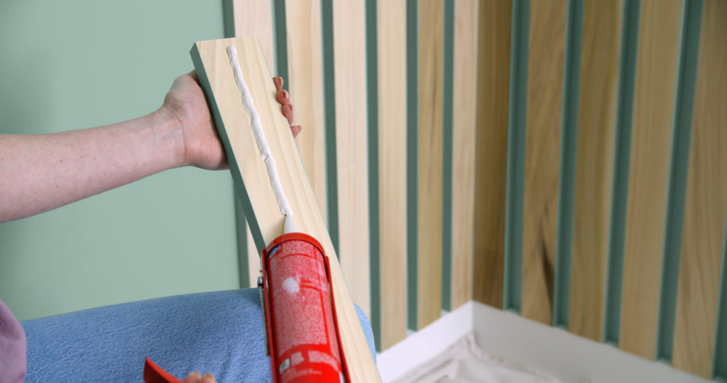 A person adding •	Construction Adhesive to the back of a wood slat.