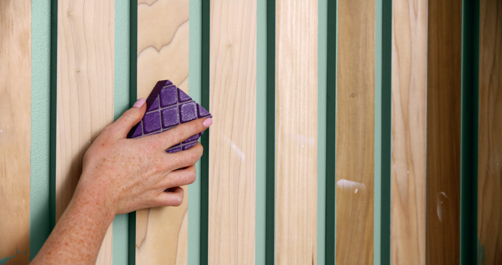 A person using a sand block to smooth out the fronts of the wood slats.