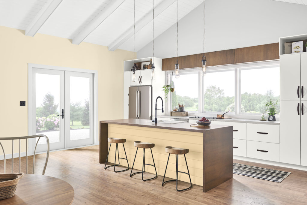 Farmhouse style kitchen with high ceiling and beams.  The walls and kitchen island are painted with a cheerful yet pleasing yellow called Corn Stalk.