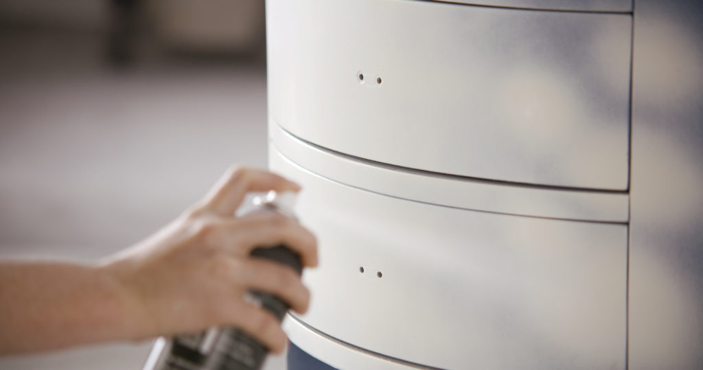 A person spray painting a nightstand with a white paint color.