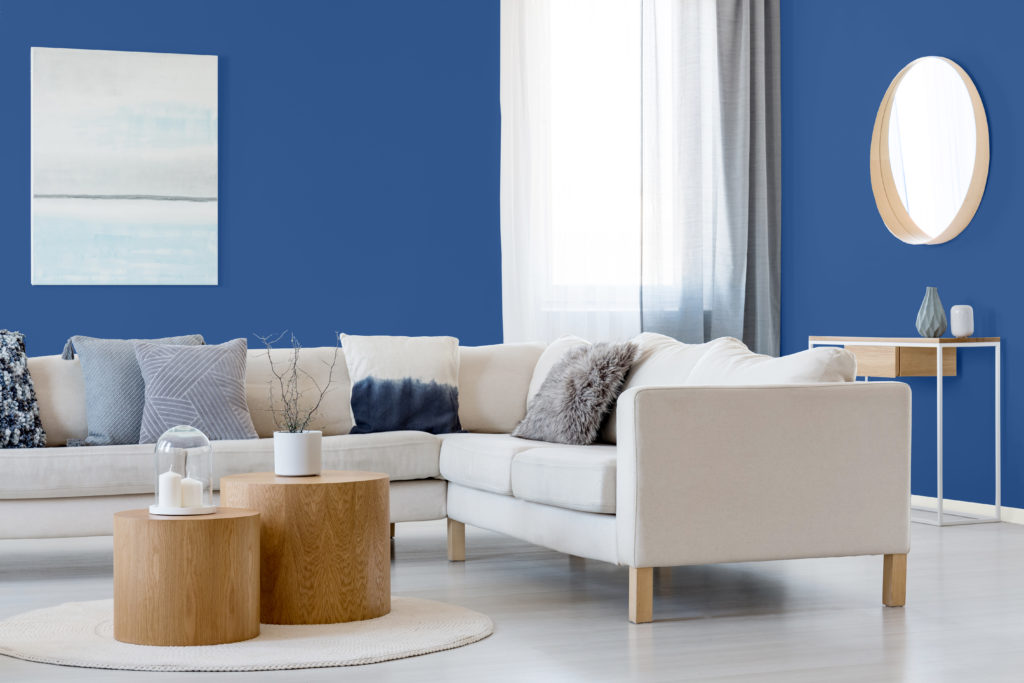 Blue and white abstract painting and mirror in wooden frame in elegant living room interior with corner sofa and coffee table