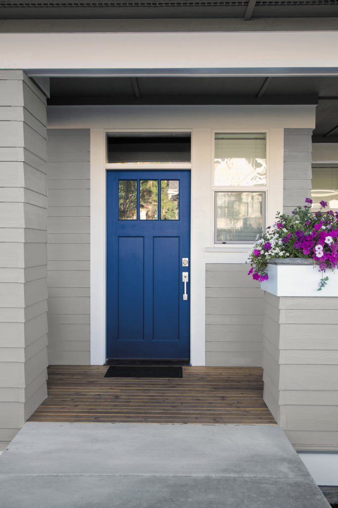 A Craftsman's style home exterior featuring the main entry area of the home. The body of the house is a mid-tone gray, the door is a bright cobalt blue  which adds a modern twist and curb appeal to house.