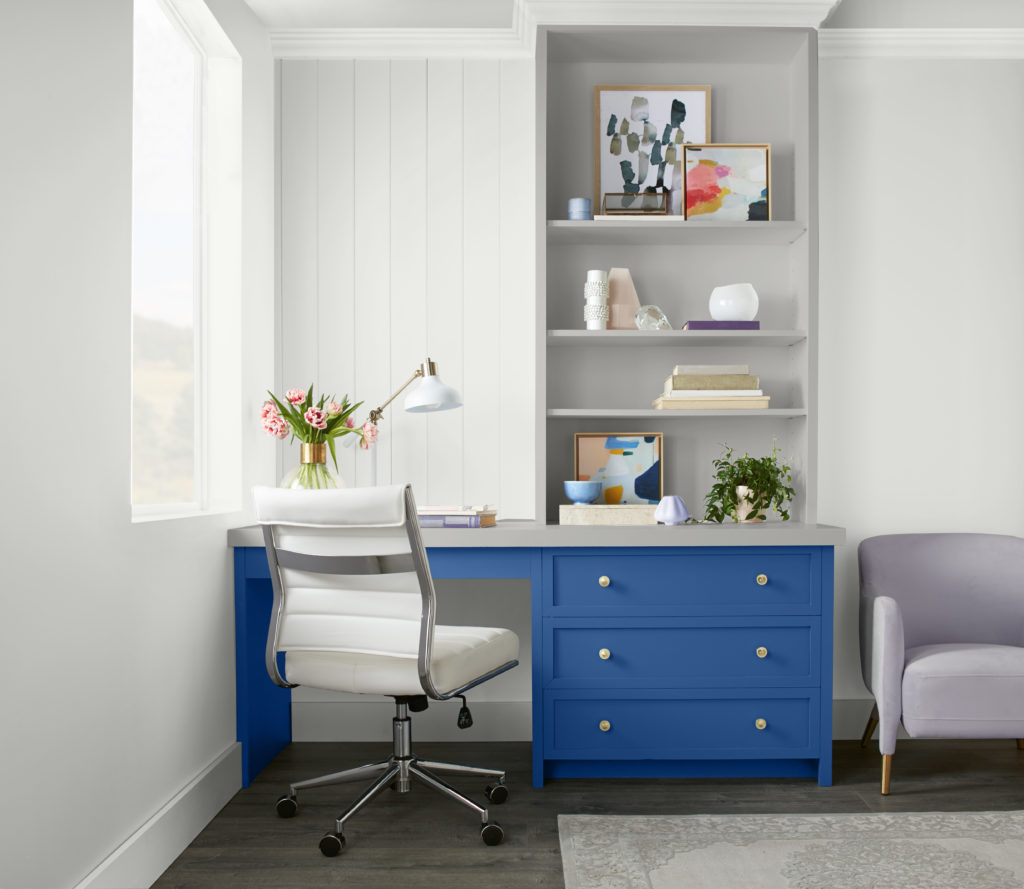 A casual home office featuring a built- in desk and shelving  area,  a bright blue accent color adds visual interest and fun to the space. 