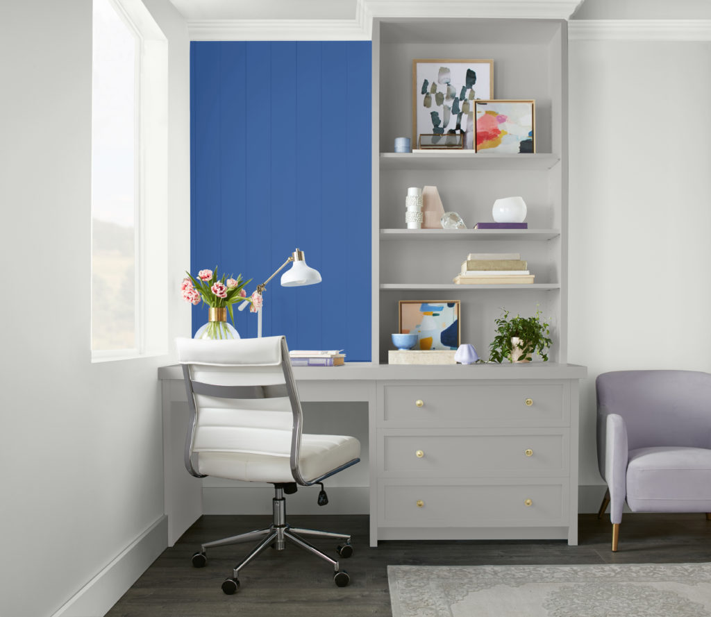 A casual home office featuring a built- in desk and shelving  area,  a bright blue color creates a focal point and highlight the vertical shiplap accent wall. 
