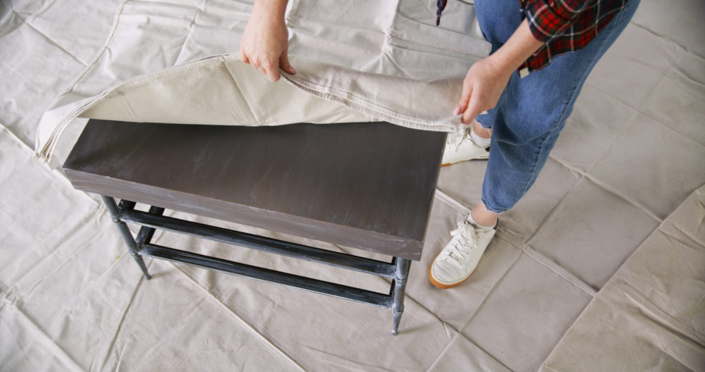 A person covering the top of the table with a drop cloth.