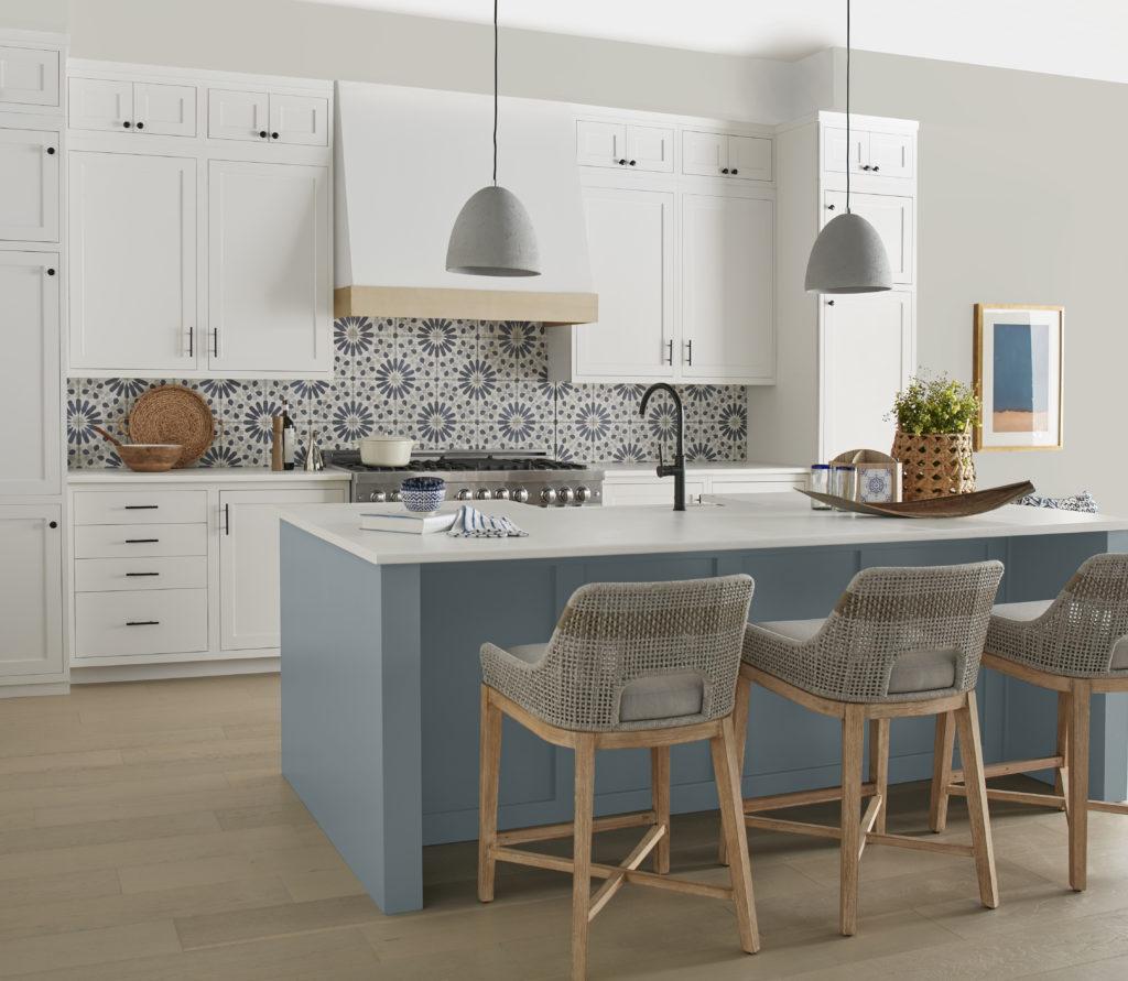 Coastal style kitchen with a blue island. The color featured on the wall is a "greige" color called Gratifying Gray. 