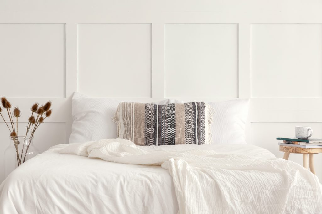 Patterned pillow on the king size bed in white simple bedroom interior in elegant apartment.