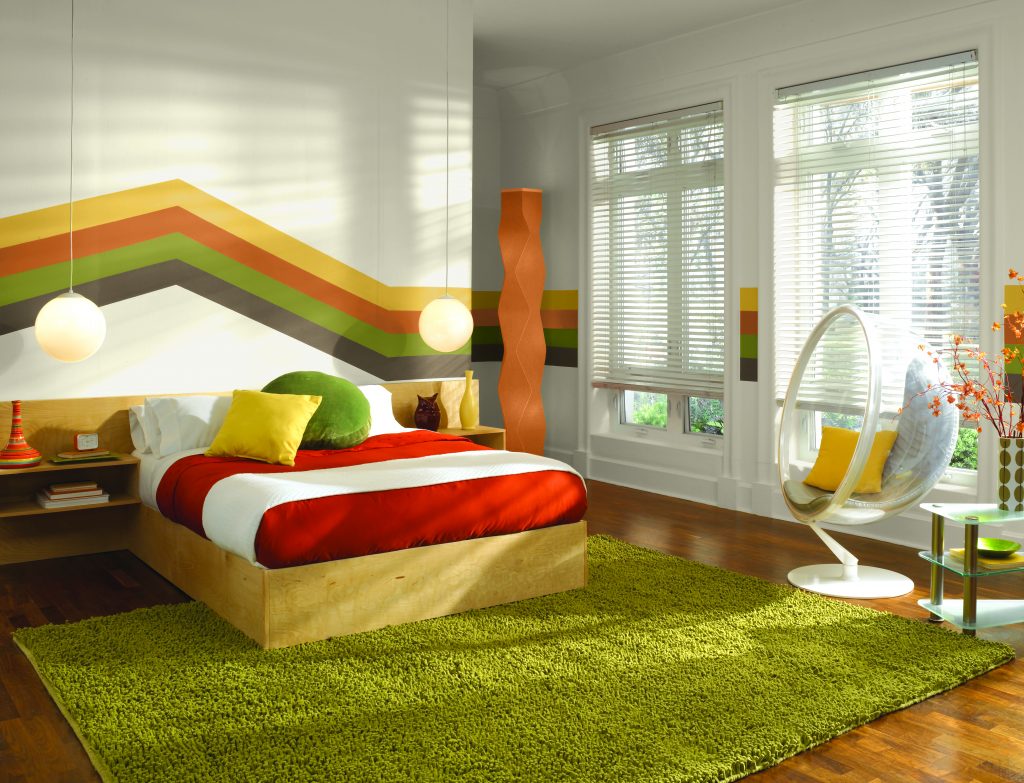 A retro inspired bedroom with a multicolor stripe wall design on the headboard wall. 