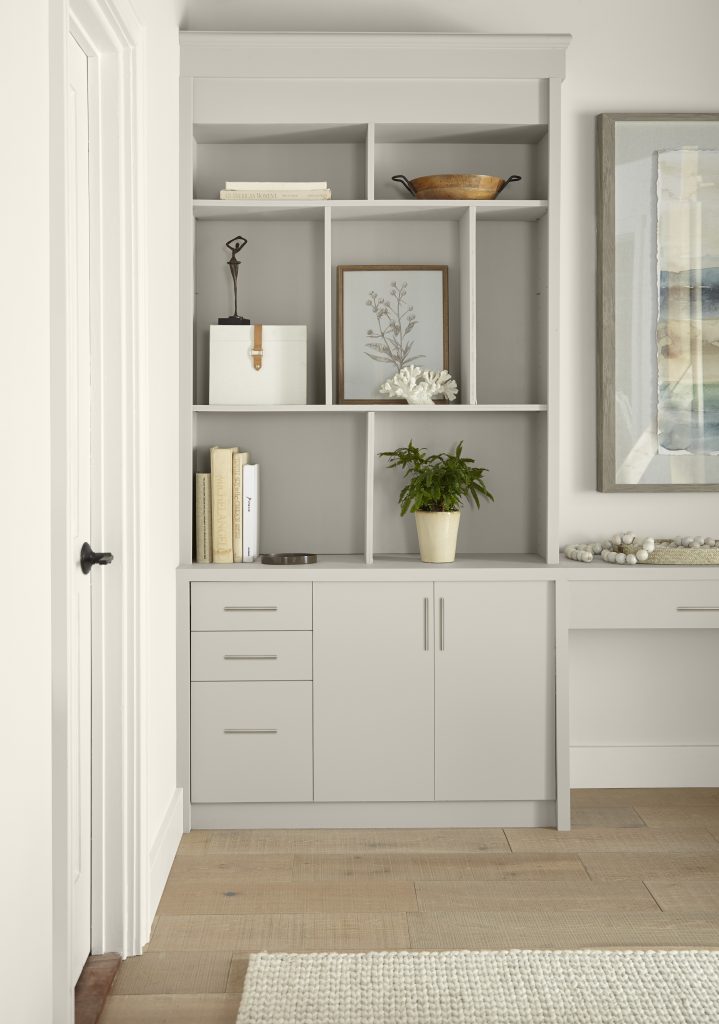 The corner of a room featuring built-in shelved painted  with a taupe-gray color called Tranquil Gray. Different décor elements are showcased on the shelves. 
