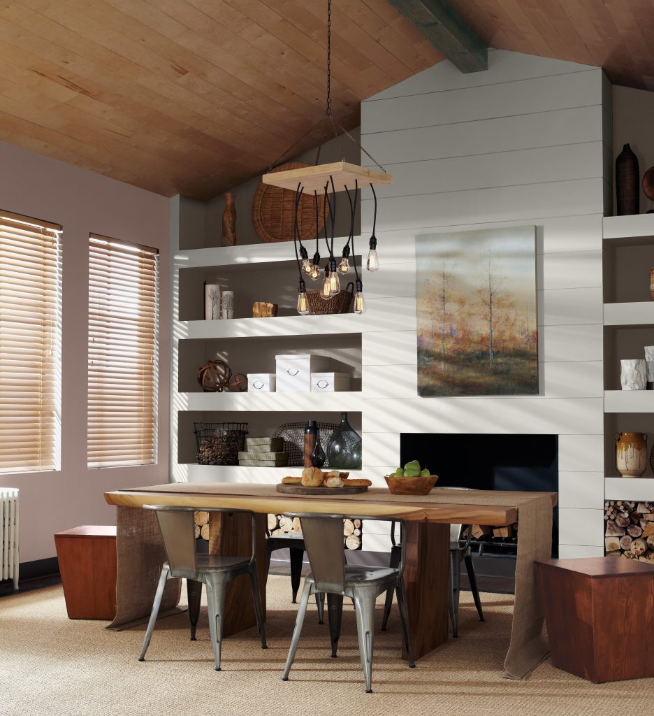 An industrial-rustic dining room with built-in shelves and fireplace. The dining table and stool are made of natural wood.  Brown paint is used on the accent wall. 