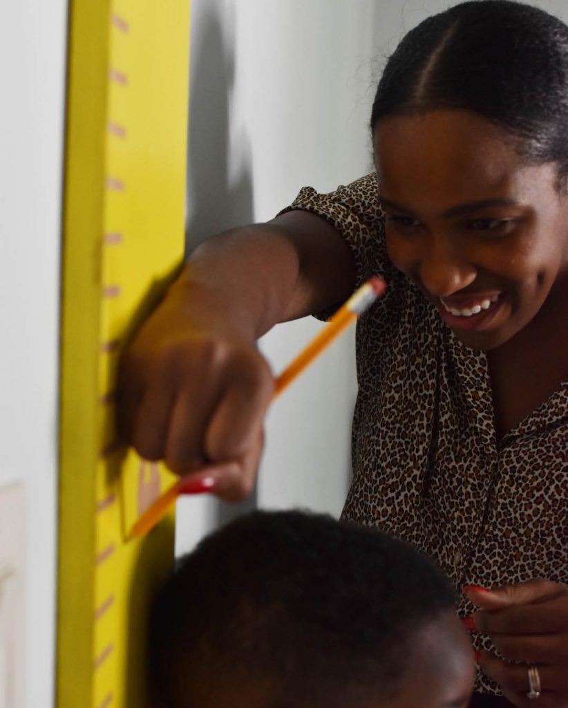 A lady with her son. She is measuring his height and marking it on the growth chart.