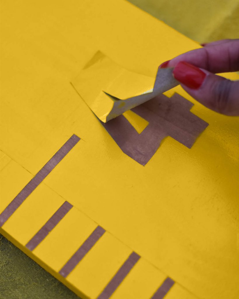 a wood plank painted in yellow with a sticker being removed to reveal stain.