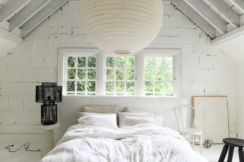 A bedroom with white painted brick walls and fluffy white bedding.