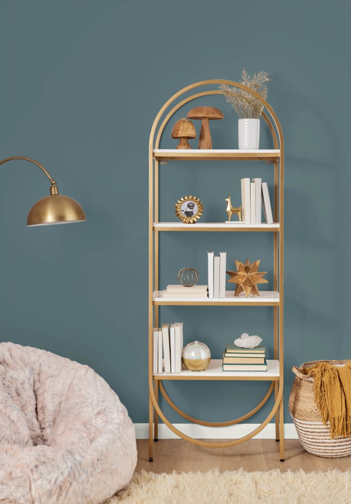 An oval bookshelf that was painted with a metallic gold spray paint.  The wall behind is a teal that allow the gold tone of the bookshelf to really pop. 