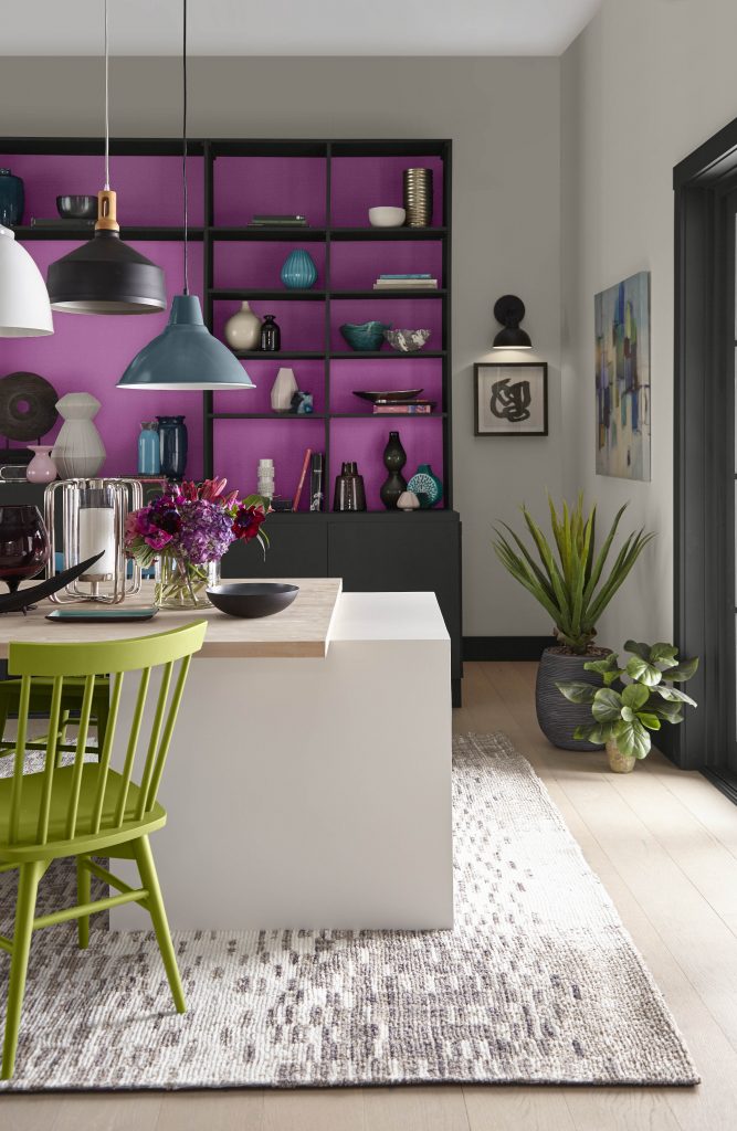 A dining area with a bright pinkish-purple hue painted on the shelf of a black cabinet.