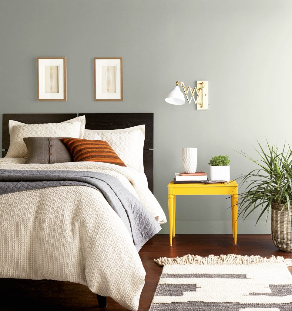 A gray bedroom with pops of yellow and orange colors used on the furniture. The Color featured on the wall is a light gray called Silver Feather. 