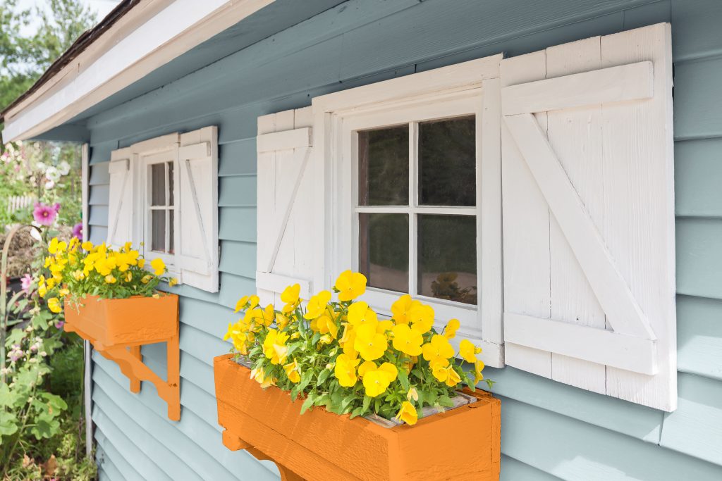 Exterior home focused on a planter box that is bright orange with planted yellow flowers.
