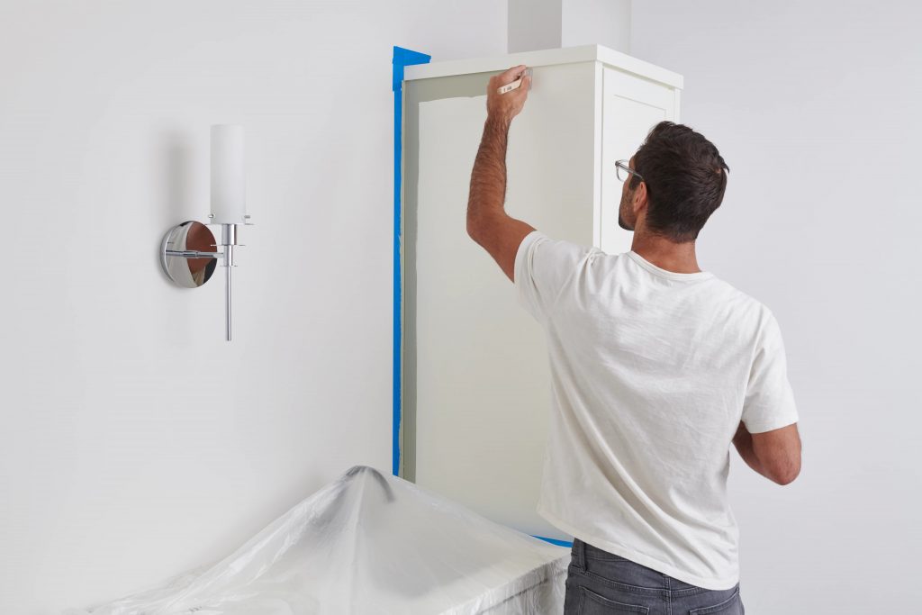 A person painting a bathroom cabinet from a white color to green.
