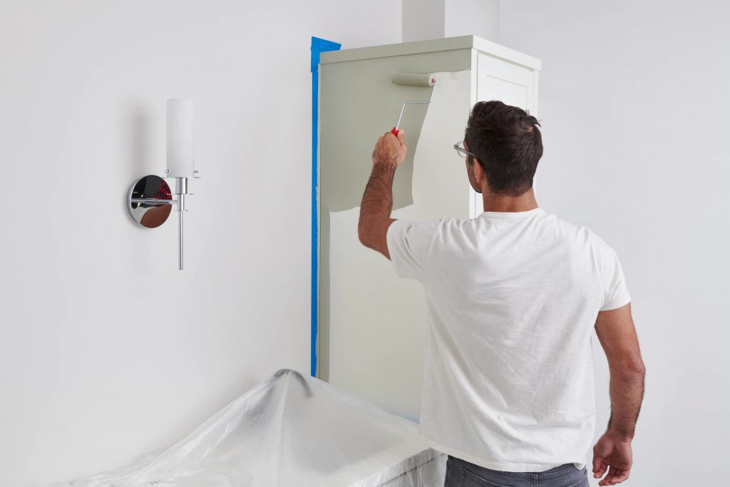 A person painting a bathroom cabinet from a white color to green.
