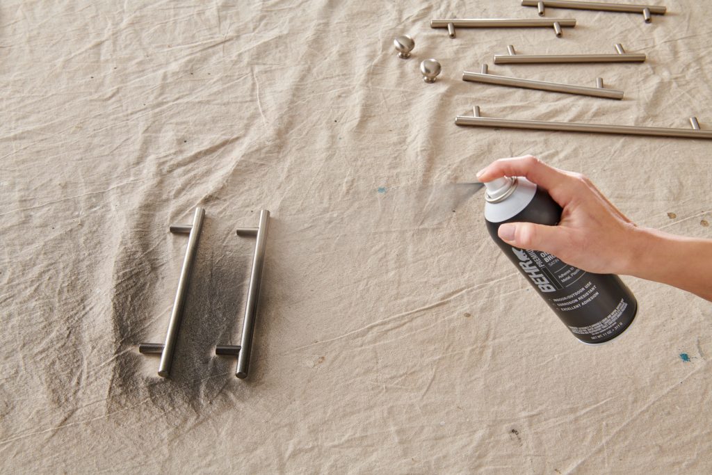 A person spray painting a silver drawer pulls to a black color.
