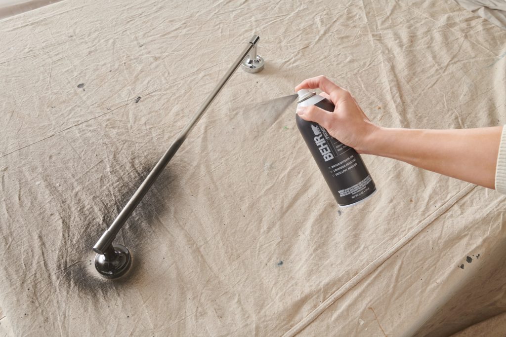 A person spray painting a silver towel bar to a black color.