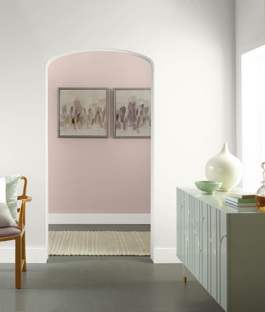 A white painted room with a hallway showing in a pink hue.