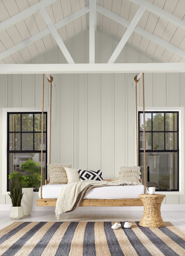 A porch with a modern wooden swing that creates and inviting area. The combination of cushions decorating the swing, creates a cozy dreamy vibe. 